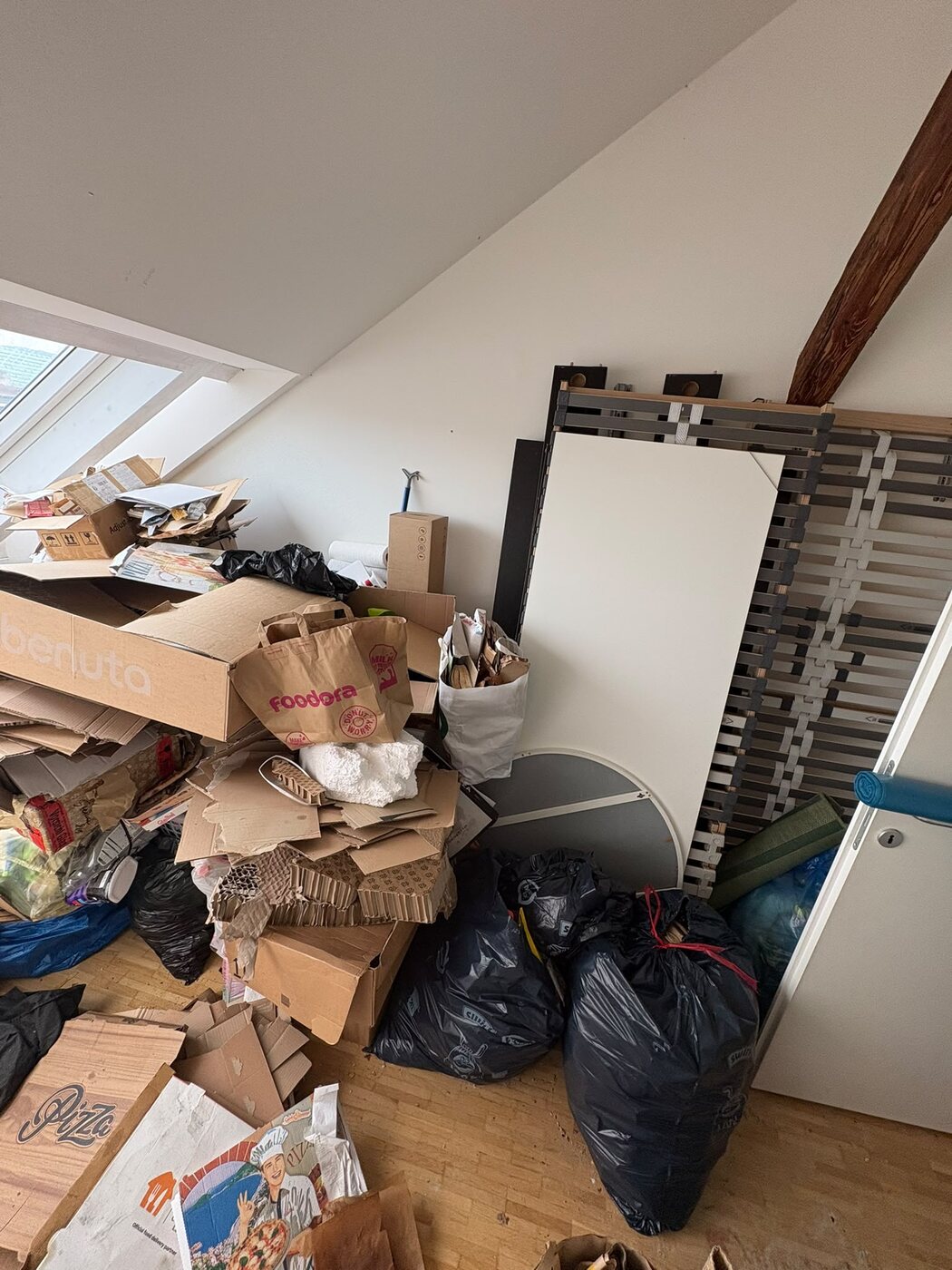 Dachzimmer mit Kartons, Pizzaschachteln und Müllsäcken vor der Räumung