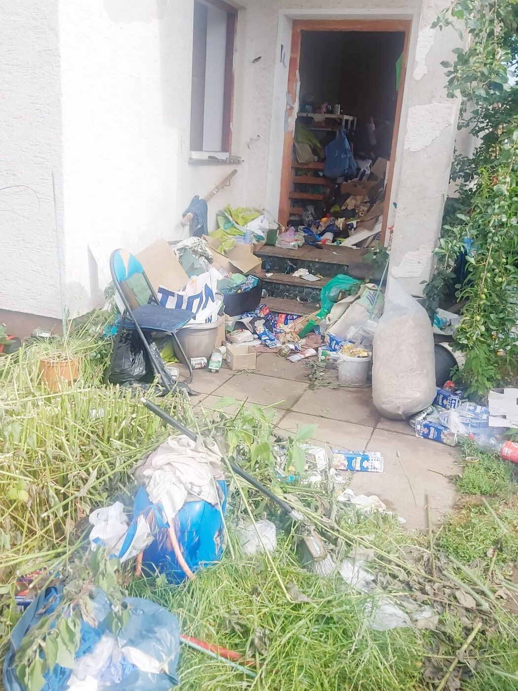 Verwilderter Hauseingang mit Müll im Garten vor der Räumung