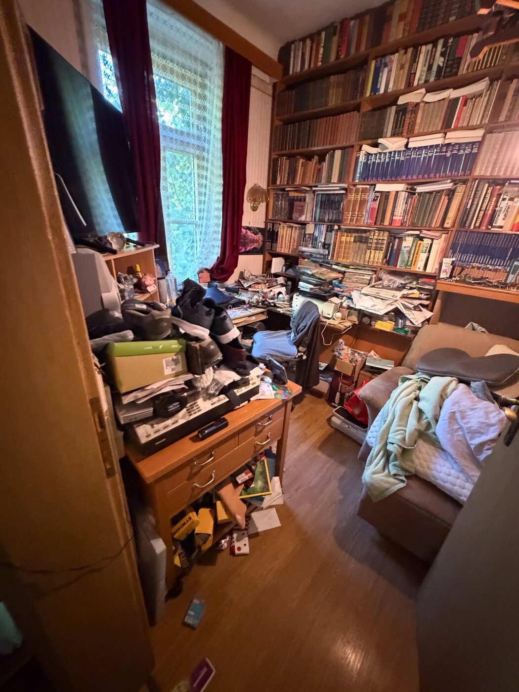 Bücherwand und Schreibtisch voller Unterlagen vor der Verlassenschaftsräumung